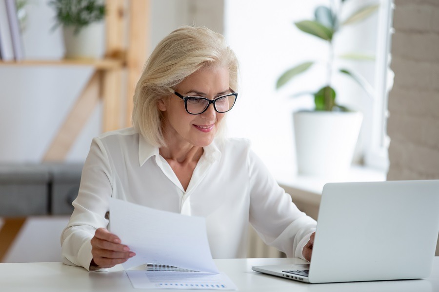 Eine Frau am Schreibtisch analysiert ein Dokument und arbeitet am Laptop - Symbolbild für die Fuhrparkanalyse