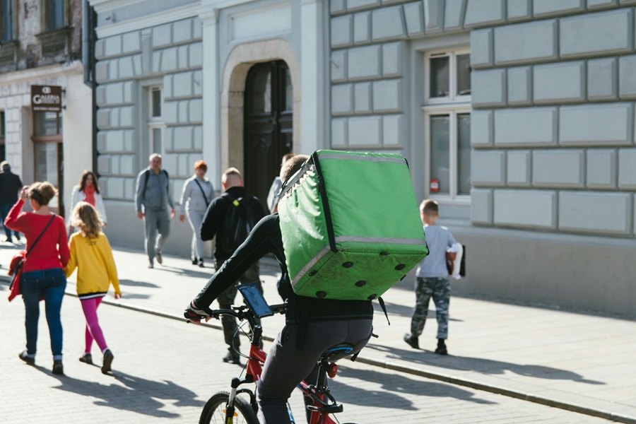 Een bezorger rijdt op een fiets met een grote groene rugzak door een druk stadscentrum. CarWise helpt bedrijven bij het integreren van fietsen in hun bedrijfsvoering.   