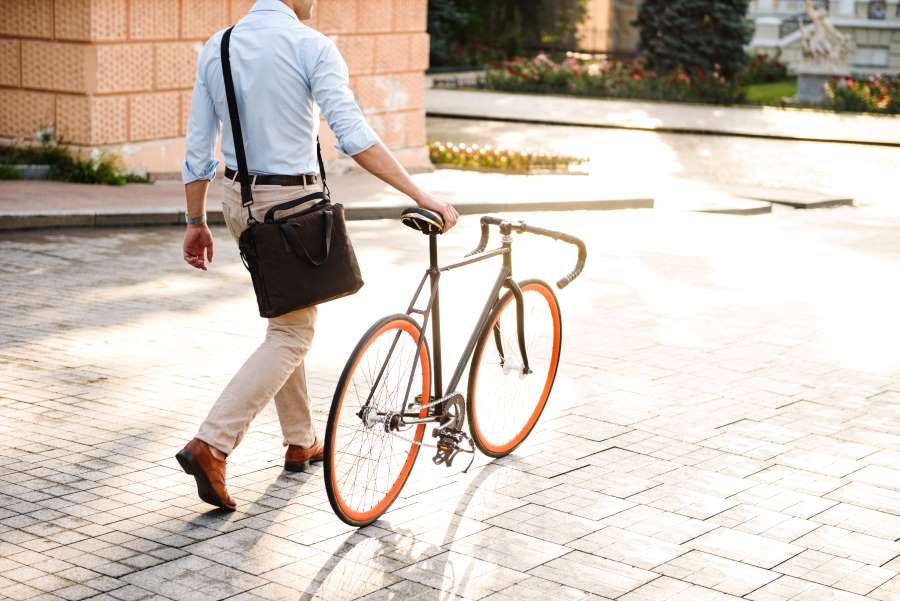 Ein Mann im Businessoutfit schiebt ein Fahrrad durch eine helle Stadtumgebung. CarWise bietet digitale Lösungen für das Mobilitätsbudget, mit denen Unternehmen individuelle Mobilität fördern, Kosten optimieren und Alternativen zum klassischen Dienstwagen flexibel in den Arbeitsalltag integrieren können.