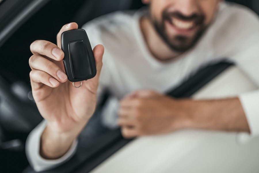 A man sits smiling in a car and holds a vehicle key up to the camera. Carano shows when pool vehicles are worthwhile and offers digital solutions for their efficient management for flexible use, reduced costs and optimal utilization in the company fleet. 
