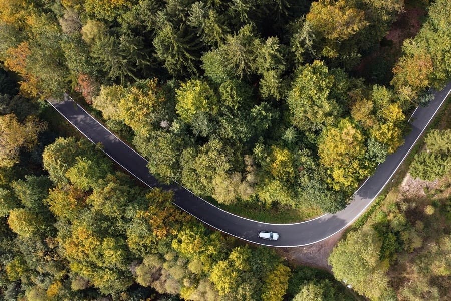 Luftaufnahme einer kurvigen Straße durch einen Wald mit einem fahrenden Auto – Symbolbild zur Frage, ob sich ein E-Auto im Fuhrpark lohnt