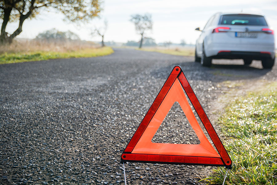 Ein Warndreieck steht auf einer Landstraße vor einem stehenden Auto, Symbol für Panne oder Unfall. Carano unterstützt Fuhrparkleiter mit digitalen Lösungen für effizientes Schadenmanagement, rechtssichere Abläufe und geringeren Verwaltungsaufwand im Fuhrpark für mehr Kontrolle und Sicherheit im Unternehmensalltag.