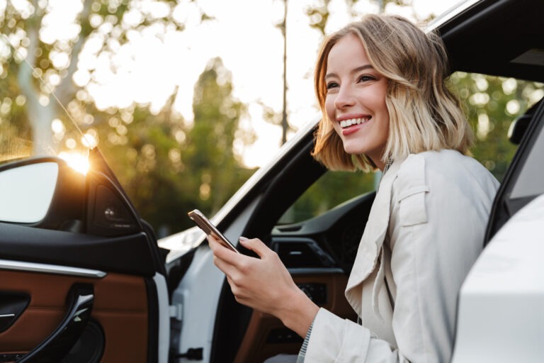 Lächelnde Frau mit Smartphone steigt in einen Firmenwagen und nutzt digitales Corporate Carsharing Software von CarWise für flexible Mobilität im Fuhrpark.