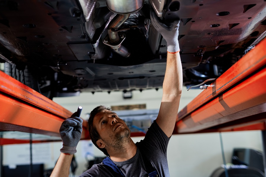 An employee uses a flashlight to check the underbody of a vehicle on a lifting platform. Regular maintenance is part of professional fleet organization. Carano offers digital solutions for planning, documentation and coordination of all processes - for greater safety, efficiency and transparency in fleet management.  