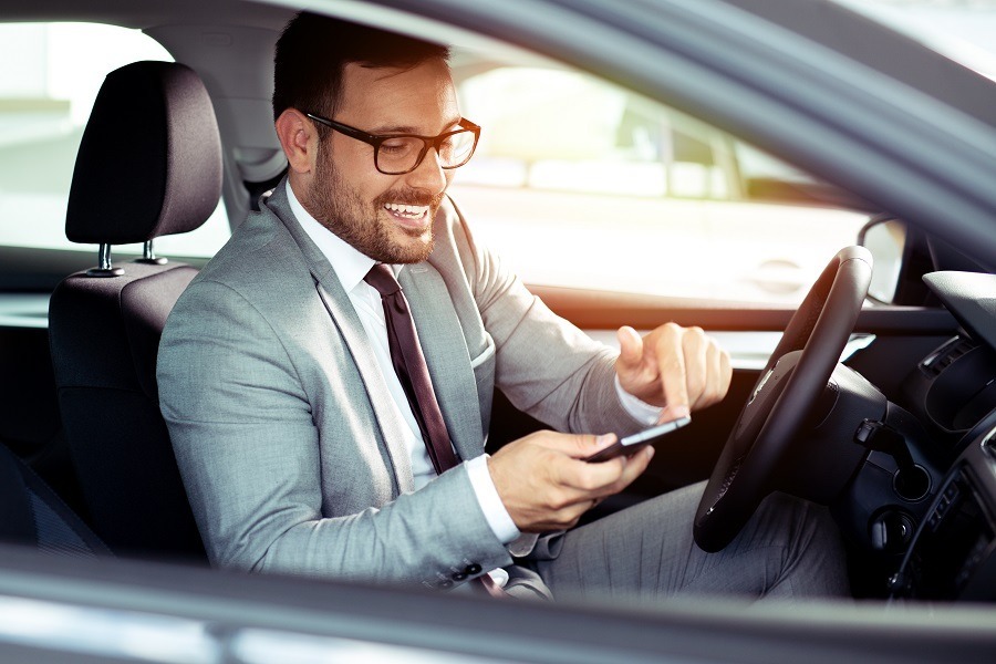 Ein Mann im Anzug sitzt im Auto und nutzt sein Smartphone. Arbeitgeber müssen regelmäßig die Führerscheine dienstlich genutzter Fahrzeuge prüfen. Carano bietet eine digitale Lösung zur gesetzeskonformen Führerscheinkontrolle mit automatisierten Erinnerungen, sicherer Dokumentation und effizientem Fuhrparkmanagement – mobil, benutzerfreundlich und rechtssicher.