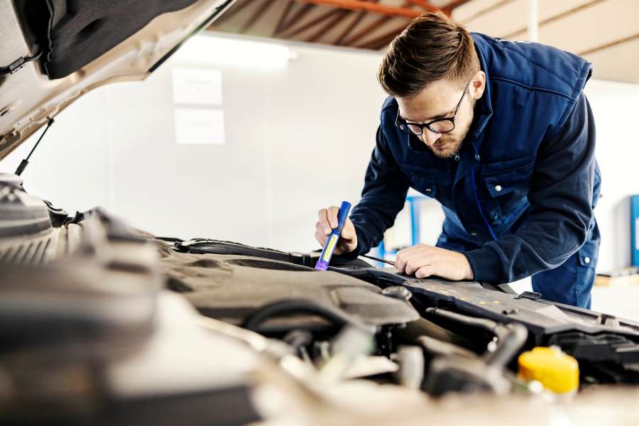 Ein Techniker untersucht den Motorraum eines Fahrzeugs mit einer Taschenlampe. Wartung und Reparaturen beeinflussen die Kosten Firmenwagen für Arbeitgeber erheblich. Carano bietet digitale Lösungen zur Planung, Dokumentation und Optimierung aller fuhrparkbezogenen Ausgaben – für mehr Transparenz und Effizienz im gesamten Fahrzeugmanagement.