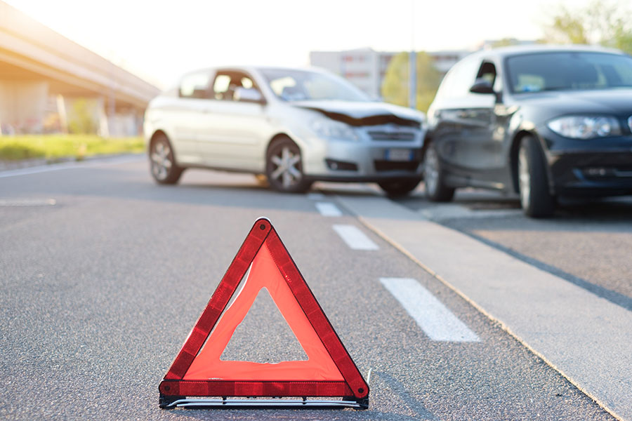 Zwei beschädigte Fahrzeuge nach einem Unfall, im Vordergrund ein aufgestelltes Warndreieck. Das Bild steht sinnbildlich für Risiken im Fuhrpark. Carano informiert über Halterhaftung und unterstützt Fuhrparkverantwortliche mit digitalen Lösungen zur rechtssicheren Fahrzeugkontrolle, um Unfälle zu vermeiden und gesetzliche Pflichten effizient zu erfüllen.