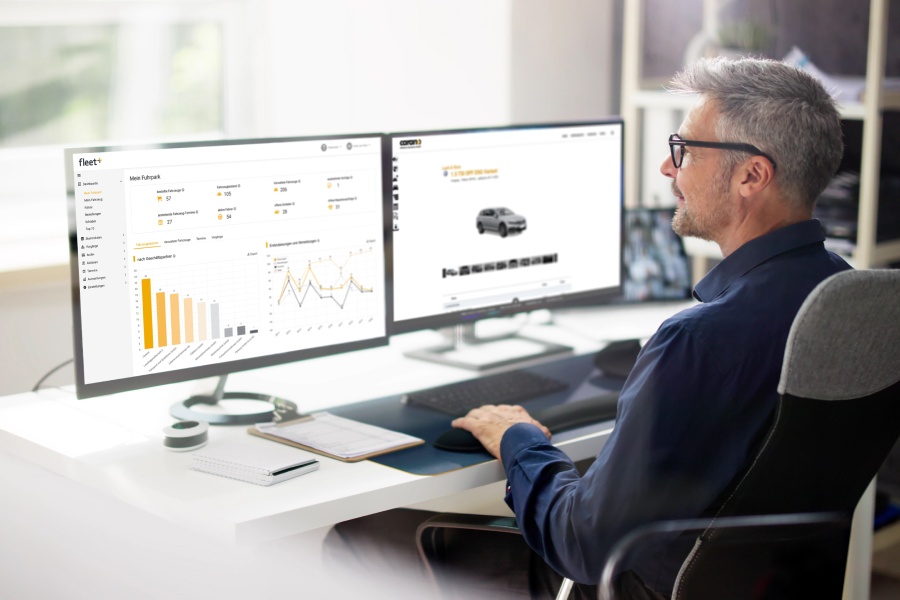 Mann works on two monitors with fleet software for analyzing vehicle data and processes. Shows a modern fleet organization with digital solutions such as Carano Fleet+ for transparent data, efficient processes and economical management of vehicle fleets. 