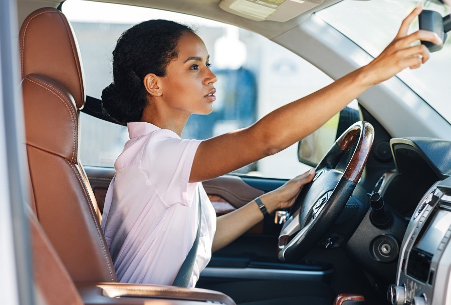 A woman sits behind the wheel of a company car with her seatbelt fastened and focuses on the rear-view mirror. Carano supports companies with digital solutions for efficient car policies and modern company car regulations - for more transparency, legal certainty and mobility in fleet management.